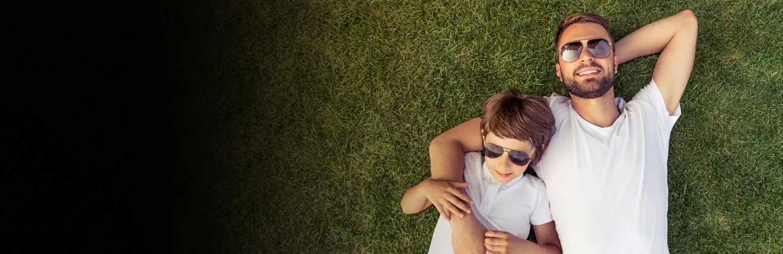 Father and son laying outside on green grass